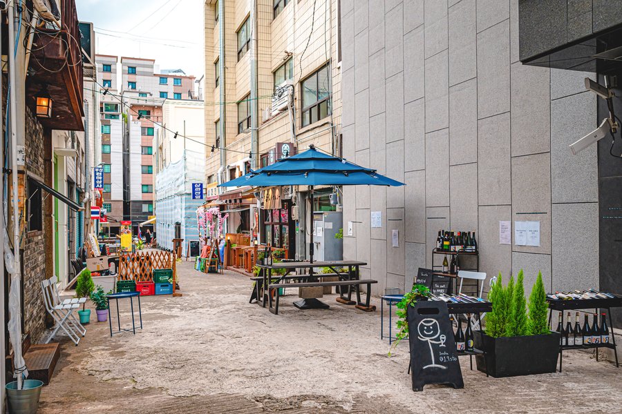 A back alley in Jeonpo Cafe Street, Busan, with a shop putting out outdoor tables and wine bottles