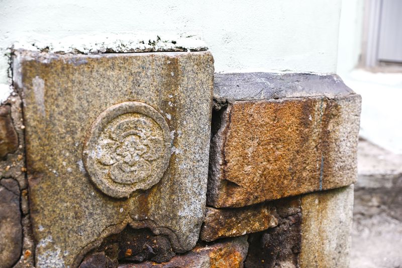 A tombstone at the corner of a wall, carved with a circular Japanese family crest.