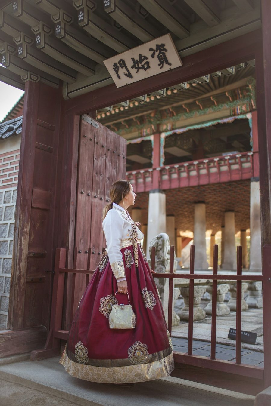 A woman in a deep-purple hanbok with gold trim standing at a palace gate