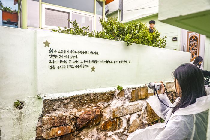 A short line of text carved into a wall, with a visitor photographing it.