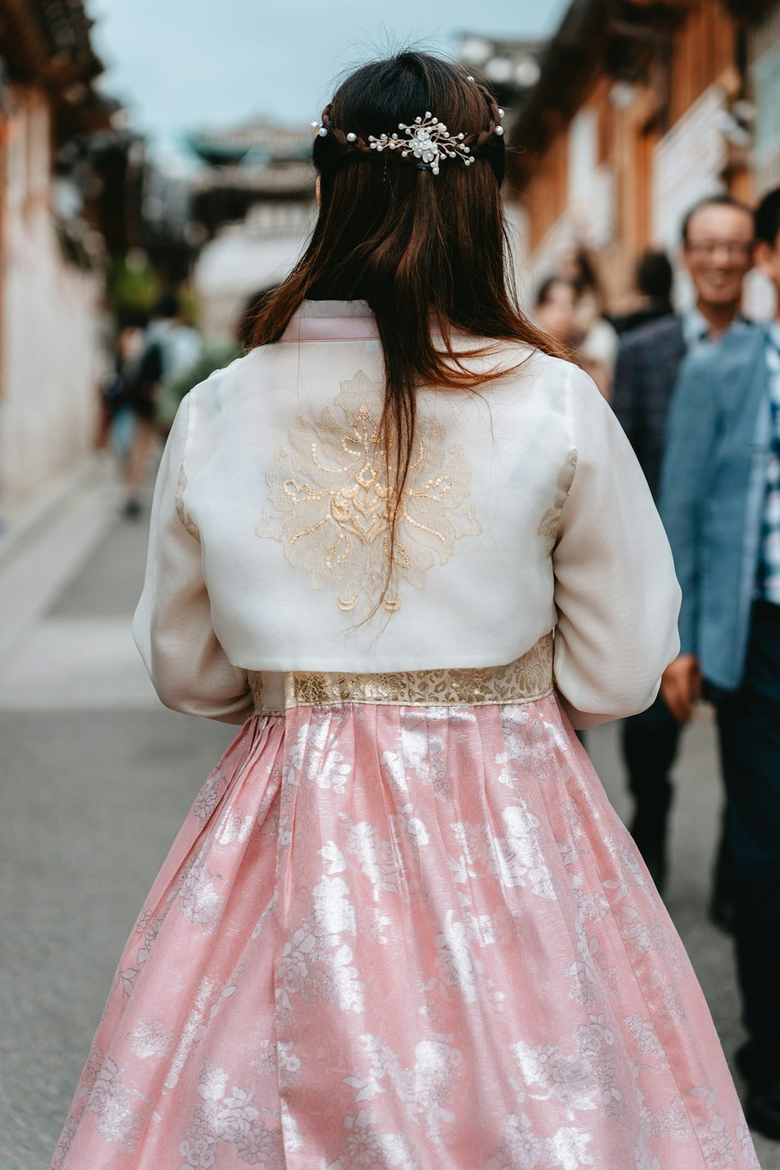 Back view of a woman in a pink hanbok walking through a traditional alley